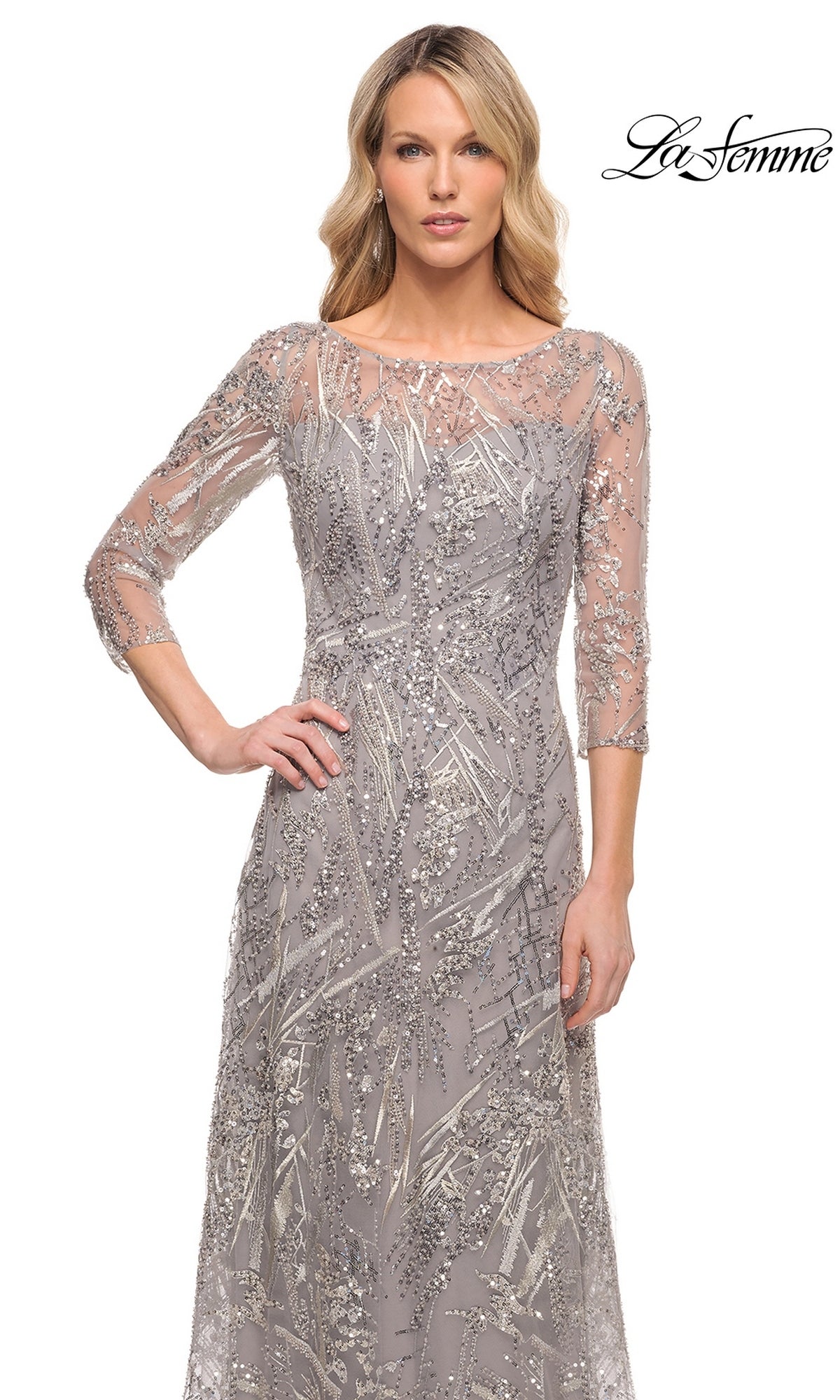 A woman wears the Long Formal Dress: La Femme 30161, a floor-length gray beaded lace dress with three-quarter sleeves and intricate silver sequin embroidery.